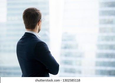 Rear back view of successful rich businessman in suit standing looking through window at modern city buildings skyscrapers thinking of future business vision, dreaming of new opportunities concept - Powered by Shutterstock