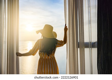 Rear back view woman opening curtains, relaxing and looking beautiful seascape panorama with rays of sun light in holiday on the balcony in high quality hotel feeling happy. Composition of nature - Powered by Shutterstock