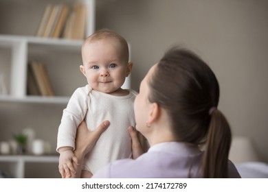 Rear back view young loving mom holding in arms her cute newborn, baby looks at camera. Family enjoy playtime together after daytime nap at home. Parent care, mothers love, infancy, motherhood concept - Shutterstock ID 2174172789