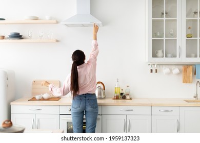 Rear Back View Of Young Millennial Housewife Choosing And Selecting Mode On Range Exhaust Hood, Pushing Button On Mechanical Fan Above The Stove, Standing In Modern Kitchen At Home