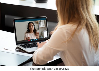 Rear back view young woman holding video call conversation with female colleague in wireless headphones, discussing working issues remotely or taking educational online class, self-isolation concept. - Shutterstock ID 1856508322