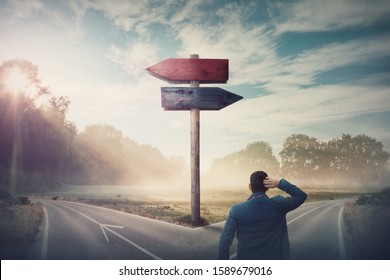 Rear businessman in front of crossroad and signpost arrows shows two different courses, left and right direction to choose. Road splits in distinct direction ways. Difficult decision, choice concept. - Shutterstock ID 1589679016