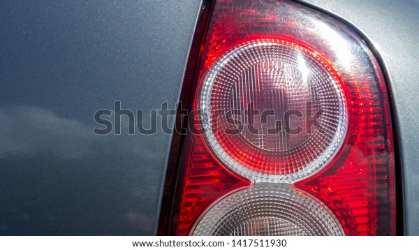Rear car, vehicle\
tail light cluster including stop light with metallic grey paint\
taken on a warm sunny day.