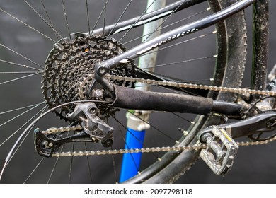 The Rear Derailleur Of A Mountain Bike Is A Close-up On A Black Background. Mountain Bike Repair In The Workshop. Dirty Mountain Bike After The Competition.