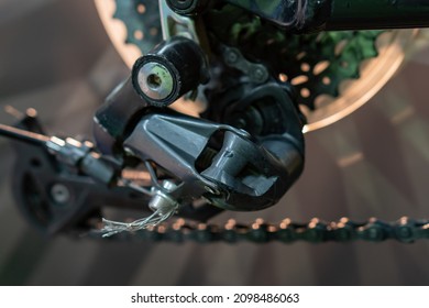 The Rear Derailleur Of A Mountain Bike Is A Close-up On A Black Background. Mountain Bike Repair In The Workshop. Dirty Mountain Bike After The Competition.