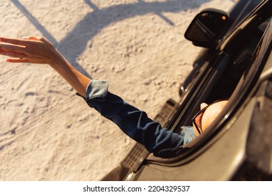 Rear High Angle View Of A Caucasian Woman Inside An Open Top Car, Waving Her Hand From The Window. Weekend Beach Vacation, Lifestyle And Leisure.