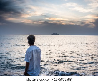 Rear of man standing by water at beach against cloudy sky
