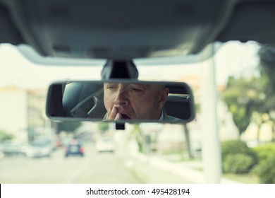 Rear mirror view reflection sleepy tired fatigued yawning exhausted young man driving his car in traffic after long hour drive. Transportation sleep deprivation accident concept