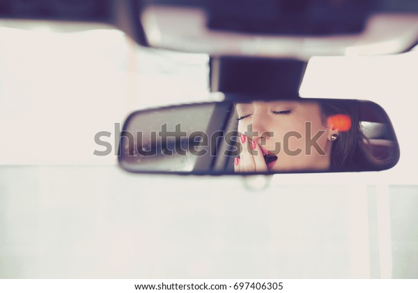 Rear mirror view reflection sleepy\
yawning woman driving her car after long hour\
drive.