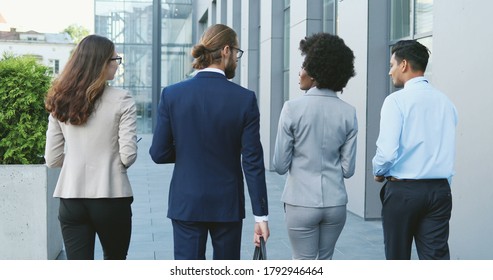 Rear of mixed-races young people in business style walking the street and talking. Multiethnic business white-collars males and females going to work in morning and chatting. Men and women. Back view.