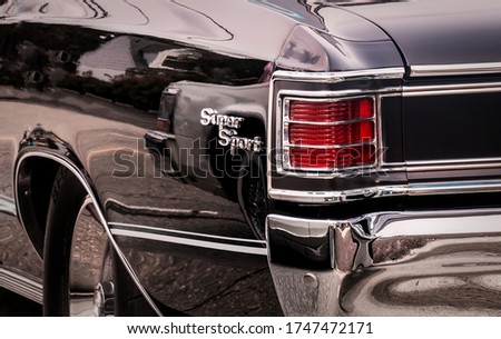 Rear part of exterior of a black old timer luxury sports car with tail lights in chrome frames and shiny chrome bumper.