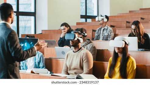 Rear of professor having speech in front of mixed-races students in VR glasses and laptops. Multiethnic males and females studying in technologic high school and listening to teacher at seminar. - Powered by Shutterstock