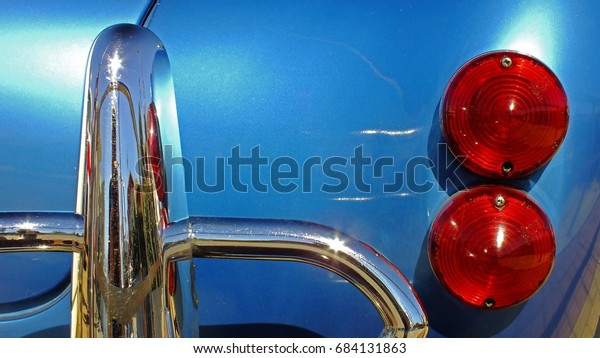 Rear right side\
of light blue classic car showing part of the chrome bumper and the\
twin circular rear lights