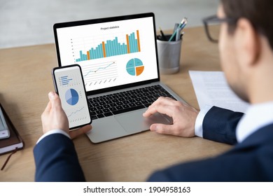 Rear shoulder view focused young male ceo executive manager using modern technology gadgets analyzing project statistics at office, smart businessman working on computer, checking data on phone. - Powered by Shutterstock