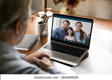 Rear shoulder view old senior middle aged man holding video call with happy young married couple grown kids and small granddaughter, enjoying pleasant conversation, distant communication concept.