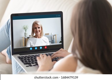 Rear shoulder view young woman relaxing on sofa, holding video call with happy mature elderly mother granny, talking chatting communicating online from home due to covid19 world outbreak quarantine. - Powered by Shutterstock