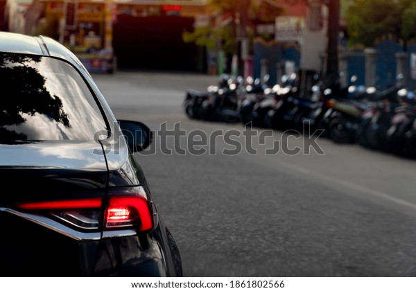 Rear\
side of black car with open brake light on asphalt road with\
blurred of motorcycle to beside. at evening\
time.