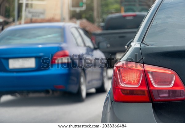 Rear side of black car with turn on brake light on\
the road in traffic junction. Various cars that park in a queue and\
run through a lot.