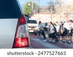 Rear side of car with turn on brake light on the road. Road crossing point with blurry image of students passing by.  Many cars had to stop to pass for safety reasons. Morning time in the city.