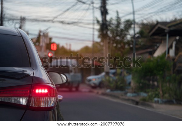 Rear side of gray car\
turn on brake light with motion of red light. Stop on asphalt road\
by traffic red  for background. Blurred another car turned left in\
the countryside.