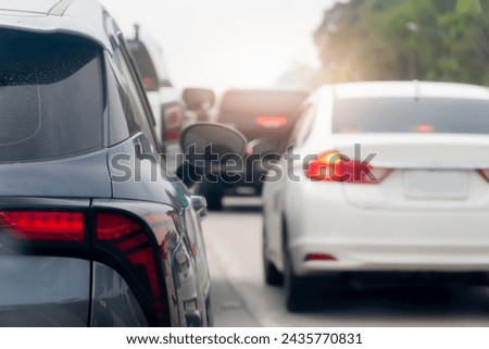 Rear side of a grey car on the road with other cars driving on the road. Blurred background of trees under white sky.