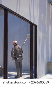 Rear Side View Of Asian Builder Worker Using Long Handle Roller Brush To Applying Primer White Paint On Cement Wall In Door Frame On Concrete Wall Inside Of House Construction Site