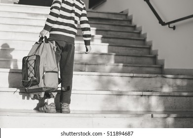 Rear side view of child carrying backpack going to or from school on outdoors background. Black and white image