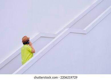 Rear Side View Of Plus Size Woman In Vintage Casual Clothing Style Talking On Smartphone While Walking Up The Stairs Outside Of White Building