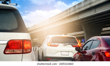 Rear Side View Of White Car With Turn On Brake Light. Traffic Conditions That Stop In A Queue At Intersections. Blurred View Of A Concrete Bridge Under The Bright Blue Sky.