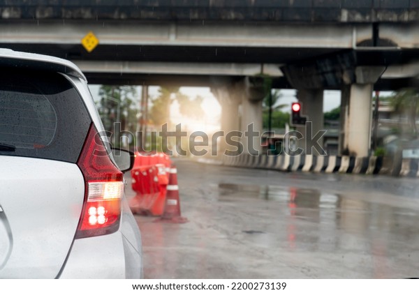 Rear side of white car with turn signal wet with\
rain. Concrete road surface wet with rainy. Parked at a red traffic\
light under a leveled bridge. Blurred water droplets from the road\
surface.
