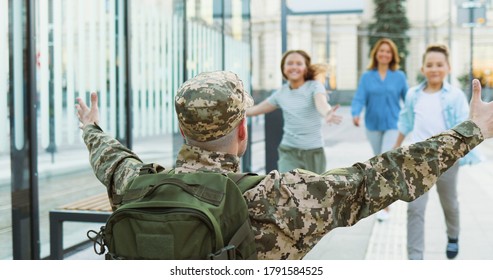 Rear of soldier in military uniform standing at train station with arms open wide and kids with wife running to hug him. Returning from army war service. Father officer meeting son, daughter and woman - Powered by Shutterstock