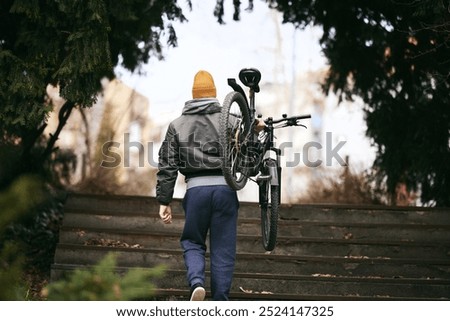 Rear view of an active middle aged man is walking up a set of steps in an urban park with his mountain bike.