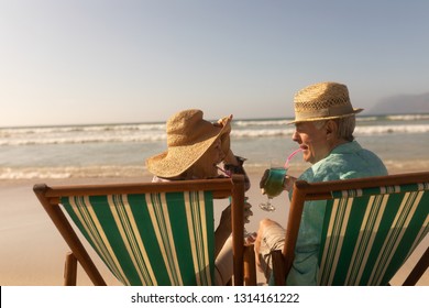 Rear view of active senior couple having cocktail drink while relaxing on sun lounger at beach - Powered by Shutterstock