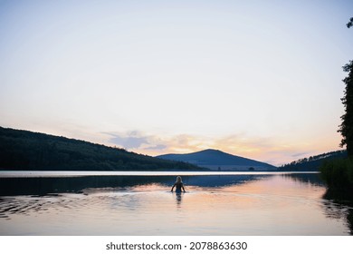 Rear View Of Active Senior Woman Swimmer Diving Outdoors In Lake, Panoramic Scene With Sunset