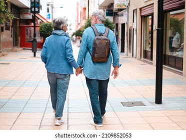 Rear view of active smiling adult Caucasian senior couple walking in the city holding hands as tourists. White-haired retired people dressed in denim enjoying freedom, walking, vacation and travel - Powered by Shutterstock