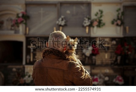 Rear View of adult man hugging small dog in cemetery
