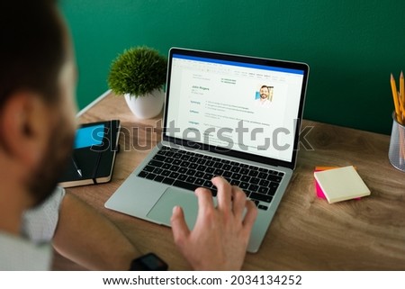 Rear view of an adult man searching for a new job and working on writing his resume on the laptop