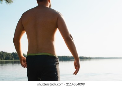 Rear View Of An Adult Strong Caucasian Man On Shore Near Water On Sunny Summer Day Outdoors. Athletic Male Swimmer Active Lifestyle, Back View. Close-up, Cropped Image.