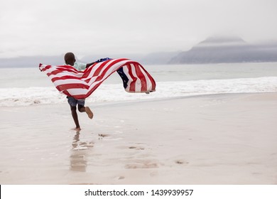 Rear view of African american boy running with American flag on the beach - Powered by Shutterstock