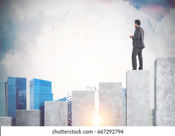 Rear view of an African American businessman holding a cup of coffee and standing on a giant bar chart looking at a cityscape. Mock up toned image - Shutterstock ID 667292794