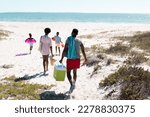 Rear view of african american family with swimming float, cooler walking at beach towards seascape. Copy space, unaltered, parents, together, childhood, picnic, nature, vacation, enjoyment, summer.