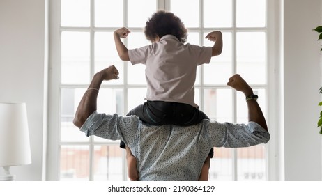 Rear View African American Father And Little Son Sitting On Dad Shoulders Showing Biceps, Strength, Healthy Lifestyle And Fit Concept, Playing Active Game, Two Superheroes, Support And Care