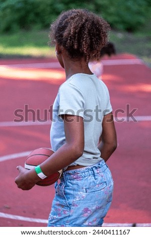 Rear view of a African American girl holding a basketball on the court, poised to play, capturing a moment of anticipation and sportsmanship, sports activities from a young age. High quality photo