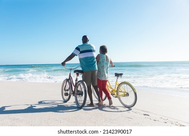 Rear view of african american senior couple wheeling bicycles at beach with copy space on blue sky. unaltered, love, togetherness, active lifestyle, enjoyment and holiday concept. - Powered by Shutterstock