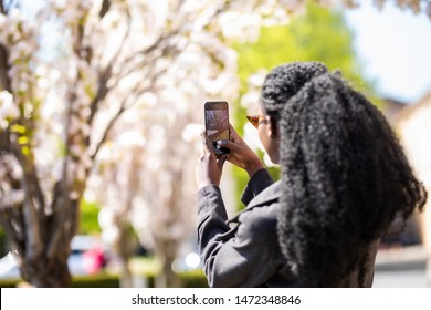 Rear View Of African American Tourist Woman Visiting A Picturesque City Street Destination, Using A Smart Phone Taking Pictures On Summer Holiday, Outdoors.