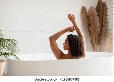 Rear View Of African American Woman Taking Bath Lying In Bathtub In Modern Bathroom At Home. Female Bathing Caring For Body Indoors. Spa, Wellness And Relaxation Concept - Powered by Shutterstock