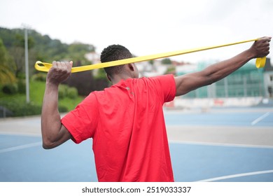 Rear view of an african sportsman stretching with elastic band standing in an outdoor basketball court - Powered by Shutterstock