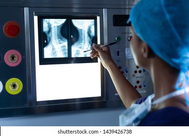 Rear view of African-american female surgeon examining x-ray of a neck pointing skeleton with pen on a light box in the hospital. Healthcare workers in the Coronavirus Covid19 pandemic
