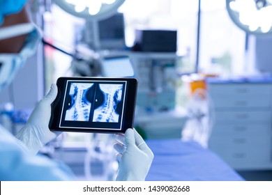 Rear view of African-american male surgeon examining x-ray of neck on digital tablet in operating room of hospital - Powered by Shutterstock