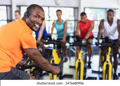 Rear view of African-american Male trainer training people to work out on exercise bike in fitness center. Bright modern gym with fit healthy people working out and training at spin class - Powered by Shutterstock